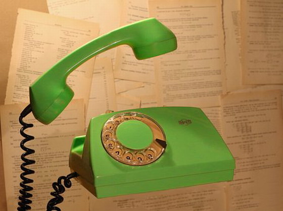 Zdjęcie przedstawia zielony telefon w stylu retro z uniesioną słuchwką i okrągłą analogową tarczą do wybierania numeru.