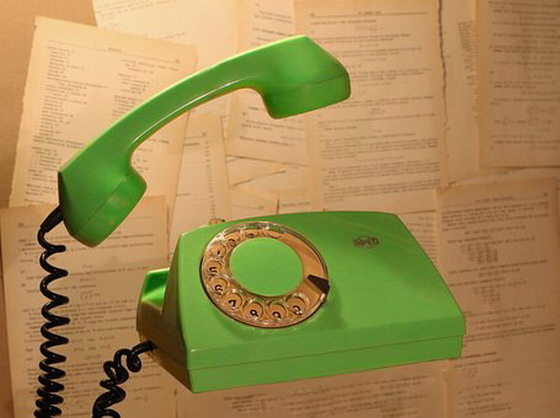 Zdjęcie przedstawia zielony telefon w stylu retro z uniesioną słuchwką i okrągłą analogową tarczą do wybierania numeru.